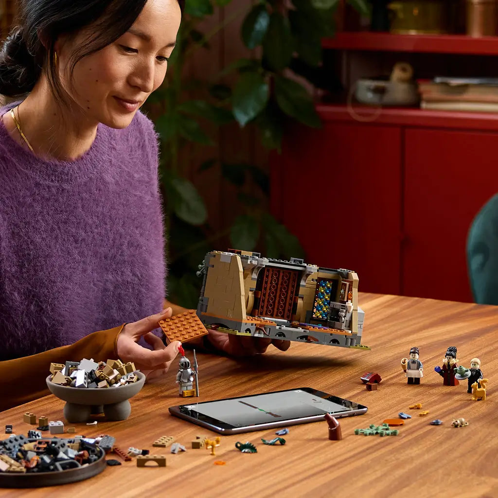 LEGO Icons Mayor Manor set 11383 build scene shows an adult assembling the gray and tan plastic mansion interior at a wood table with minifigures, pieces and a tablet.