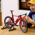 LEGO Icons Road Bike model in red and black bricks sits on a gray stand as a person adjusts the drop handlebar at a wooden table in a softly lit home interior.