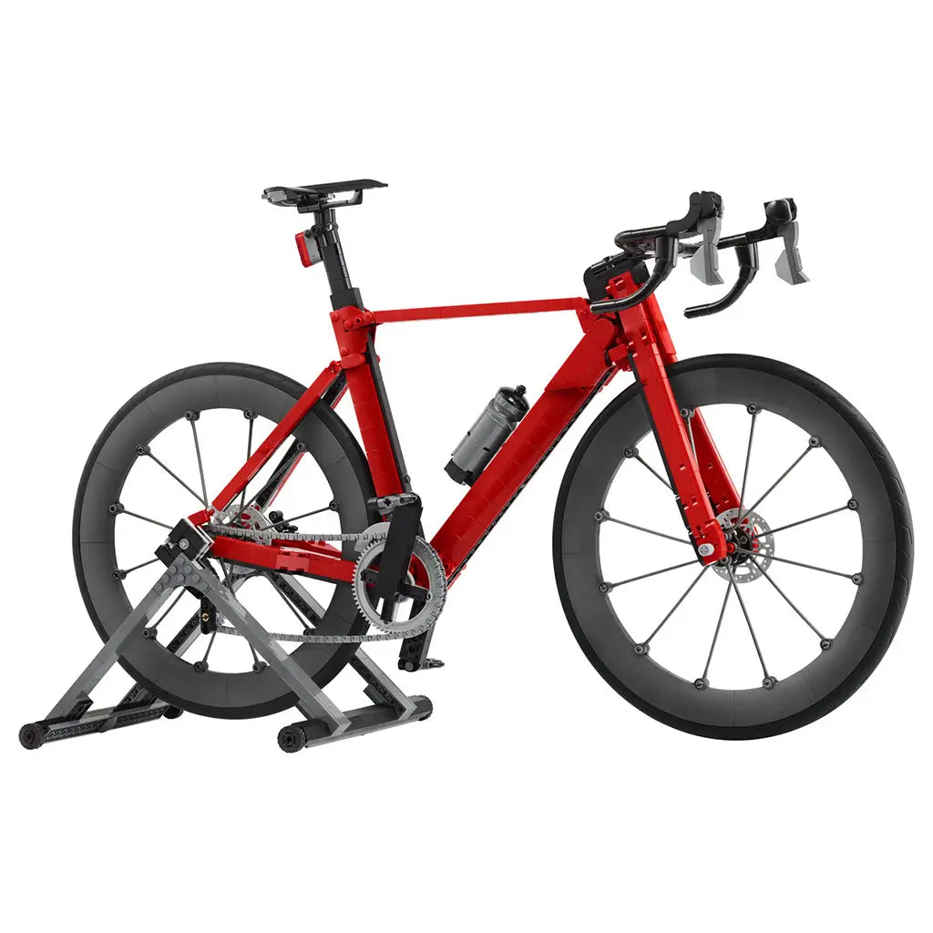 LEGO Icons Road Bike model in red and black plastic bricks, with drop handlebars, deep wheels, bottle, drivetrain and gray display stand on a clean white background.