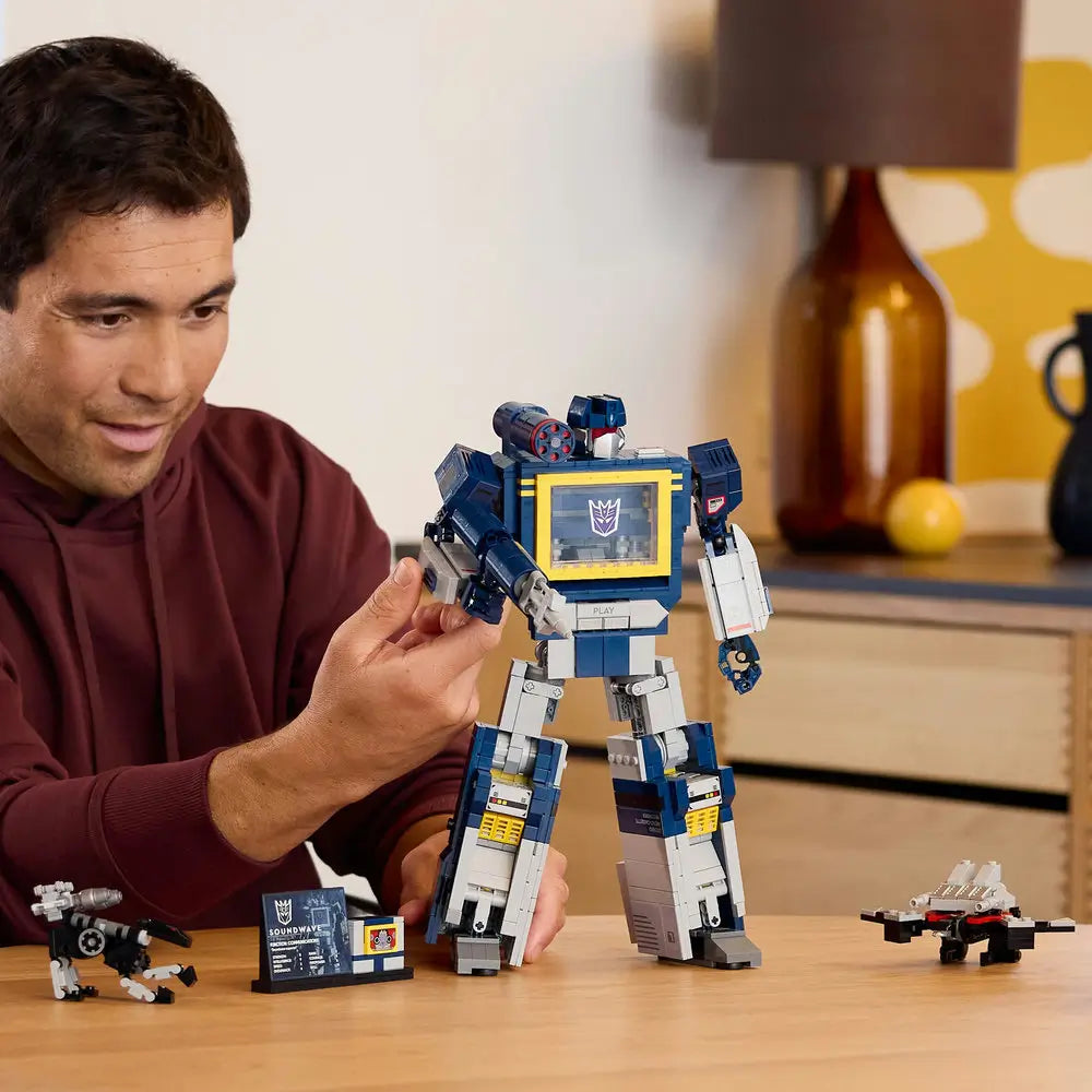 Person assembling the LEGO Icons Transformers Soundwave set, showing the blue and gray robot model with articulated limbs and accessories including cassette builds and a display plaque.