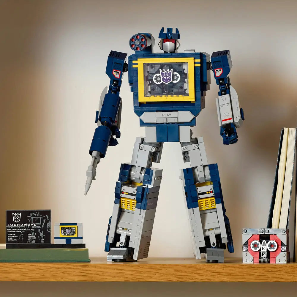 Completed LEGO Icons Soundwave model standing on a shelf with accessories including a cassette tape build, display plaque, and minion figure, replicating the classic Transformers robot design.