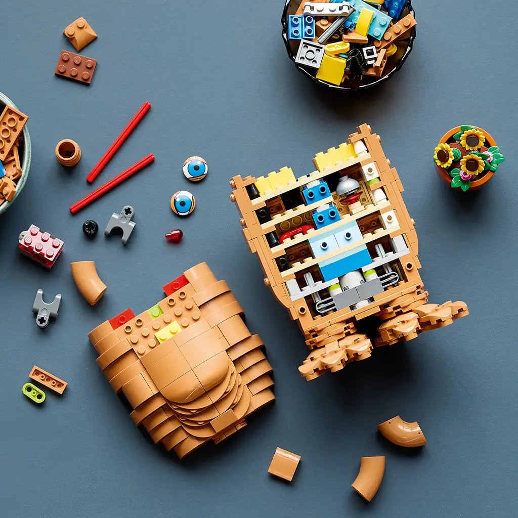 LEGO Ideas E.T. building set in tan and brown bricks is partly assembled on a dark tabletop, revealing colorful interior pieces beside blue eyes and a flowerpot.