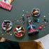 LEGO Ideas La Catrina building set in black, magenta, blue and orange bricks lies partly assembled on a dark tabletop, surrounded by bowls of pieces and floral details.