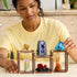 A person wearing a yellow shirt builds the LEGO Ideas Mineral Collection set, arranging translucent crystal structures in shades of blue, red, purple, and gold on wooden-style frames.