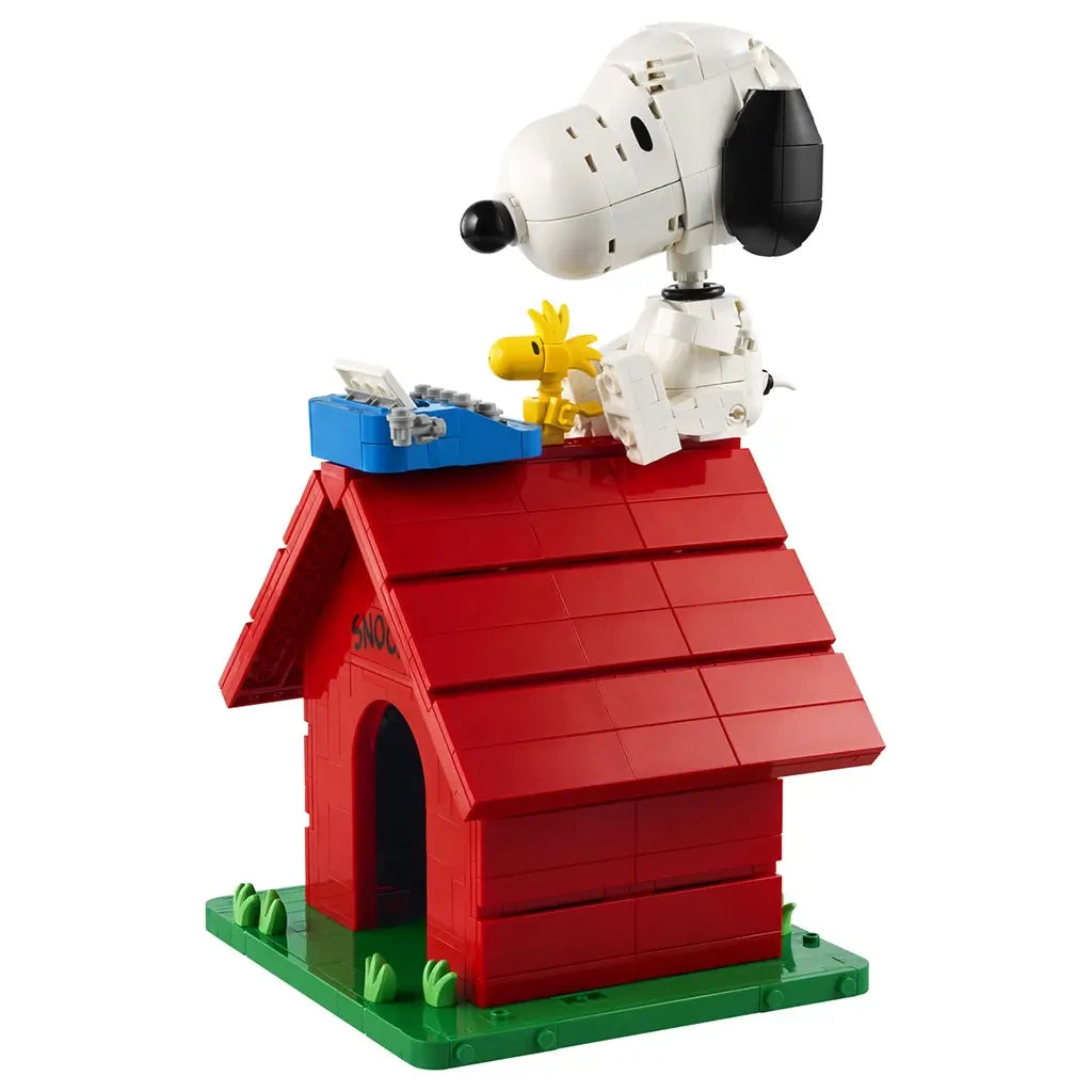 LEGO Ideas Snoopy's Doghouse model in red and green bricks features white Snoopy and yellow Woodstock with a blue typewriter on the roof, isolated against a white background.