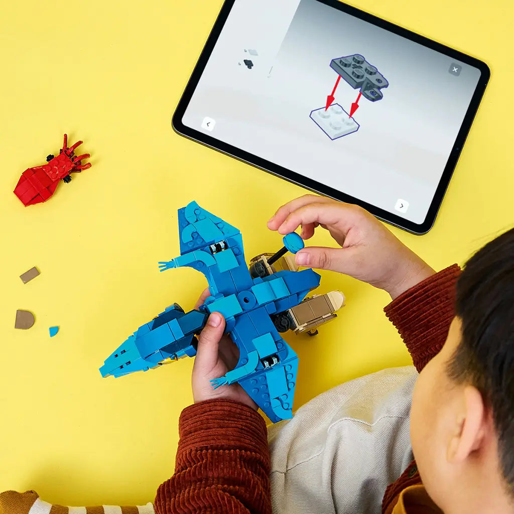 LEGO Jurassic World Baby Dinosaur Pteranodon set shows a child assembling the blue and tan brick-built flying dinosaur beside a tablet with digital instructions on yellow.