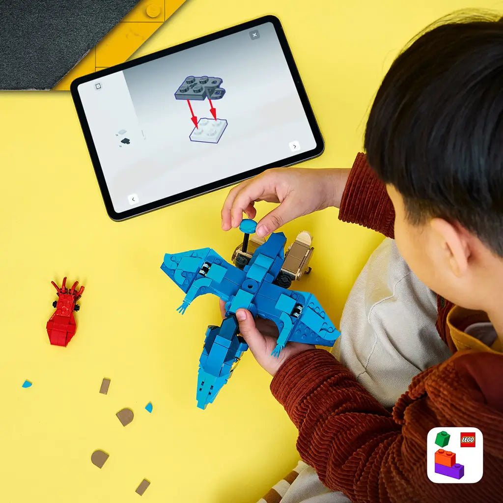 LEGO Jurassic World Baby Dinosaur Pteranodon set shows a child building the blue and tan flying dinosaur beside a tablet with digital instructions on a yellow surface.