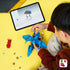 LEGO Jurassic World Baby Dinosaur Pteranodon set shows a child building the blue and tan flying dinosaur beside a tablet with digital instructions on a yellow surface.