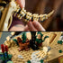 LEGO Jurassic World Triceratops fossil details use tan plastic bricks, showing the articulated tail and a prehistoric display base with plants, rocks and skeletal feet.