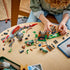 LEGO Jurassic World Spinosaurus building set covers a wood table with the gray and red dinosaur, enclosure sections, minifigures and loose bricks as a child assembles it.