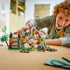 LEGO Jurassic World Spinosaurus playset shows a gray, tan and red brick dinosaur breaking through an orange and black enclosure as a child plays behind it on a wood table.