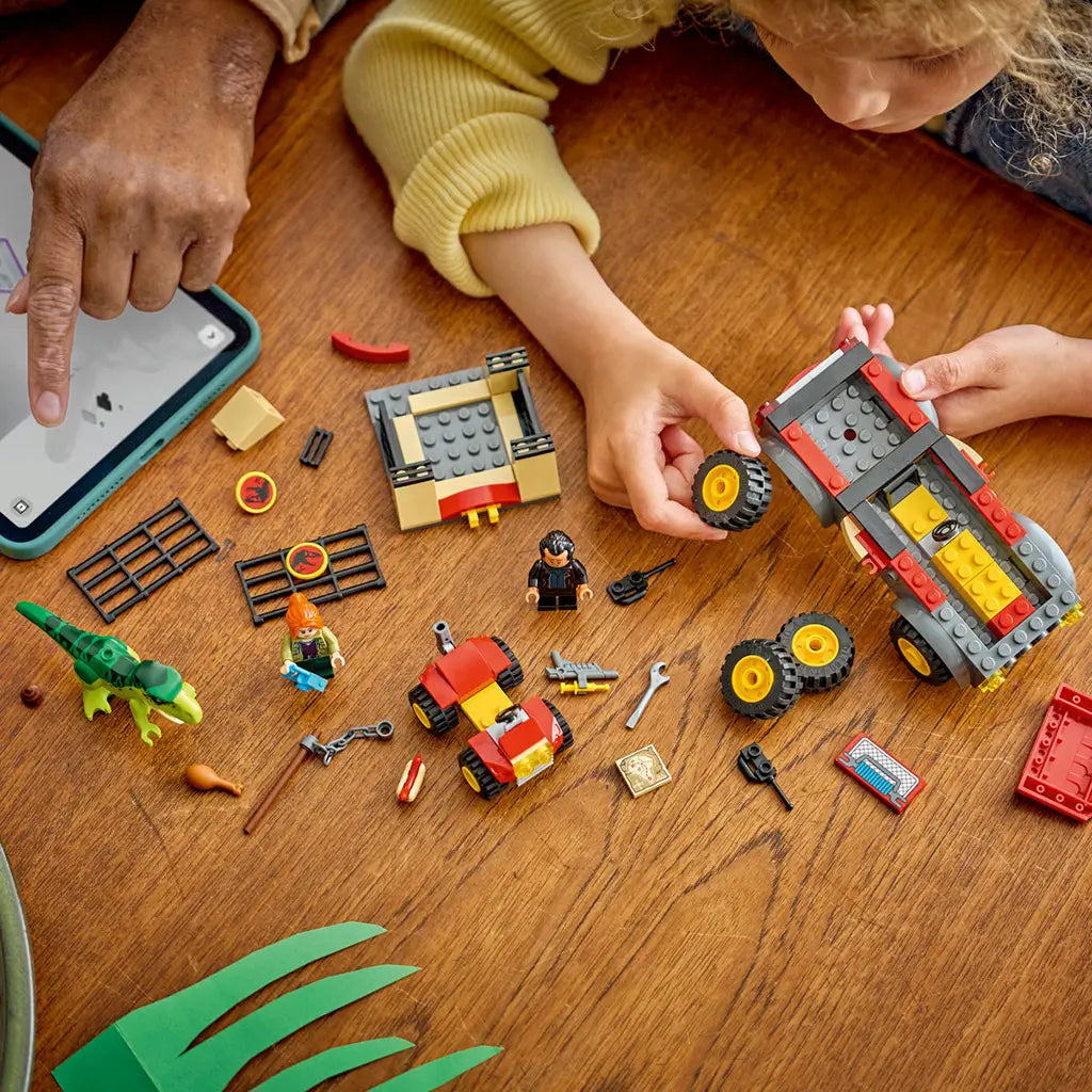 LEGO Jurassic World Young T. rex building set spreads red, gray and tan truck parts, ATV, minifigures and green dinosaur across a wooden table as a child assembles it.