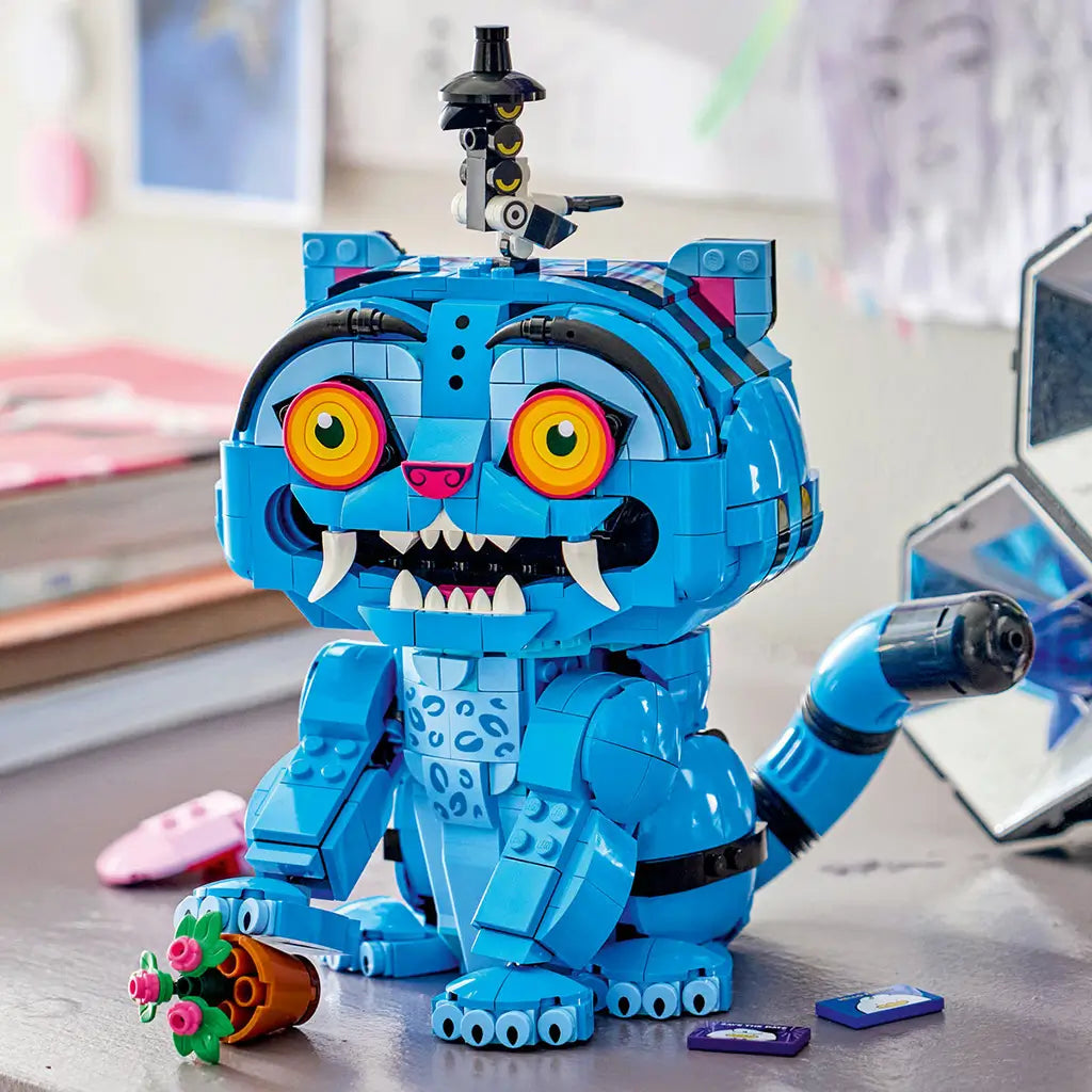 LEGO KPop Demon Hunters Derpy Tiger model uses bright blue plastic bricks with orange eyes, white fangs and a striped tail, displayed with Sussie Bird and flower pot.