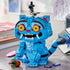 LEGO KPop Demon Hunters Derpy Tiger model uses bright blue plastic bricks with orange eyes, white fangs and a striped tail, displayed with Sussie Bird and flower pot.