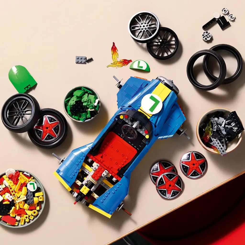 LEGO Mario Kart building set shows green, blue, yellow and black plastic pieces, wheel components and kart body sections arranged for assembly on a tabletop with parts bowls and accessories nearby.