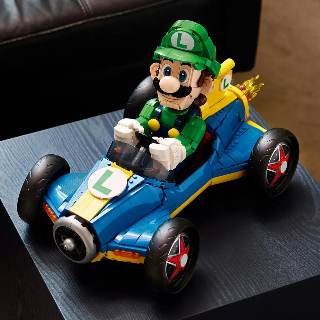 LEGO Mario Kart Luigi & Mach 8 display features bright green, blue and yellow plastic surfaces, a streamlined kart shape with oversized wheels, presented on a dark tabletop in a living room setting.