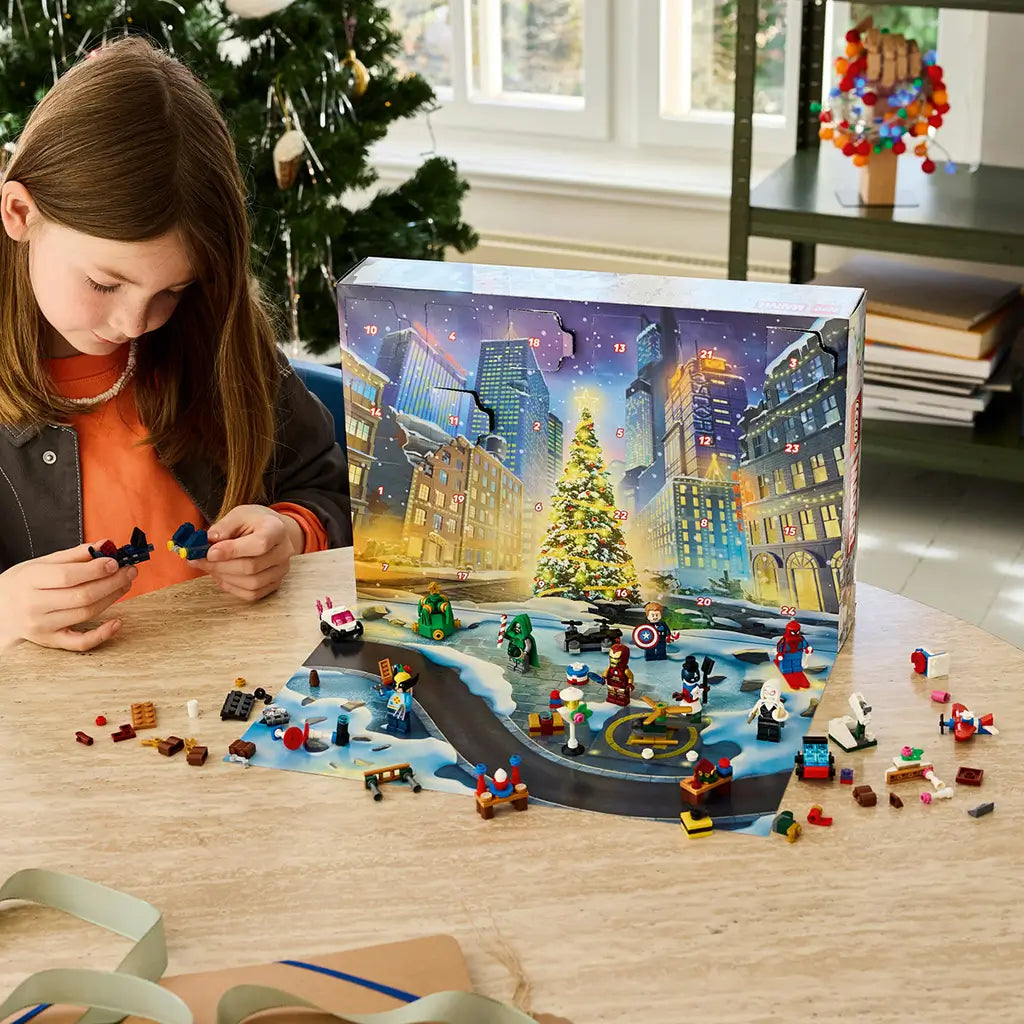 LEGO Marvel Advent Calendar 2026 playset is built by a child at a wooden table, with colorful superhero minifigures and mini builds spread before a snowy city calendar.