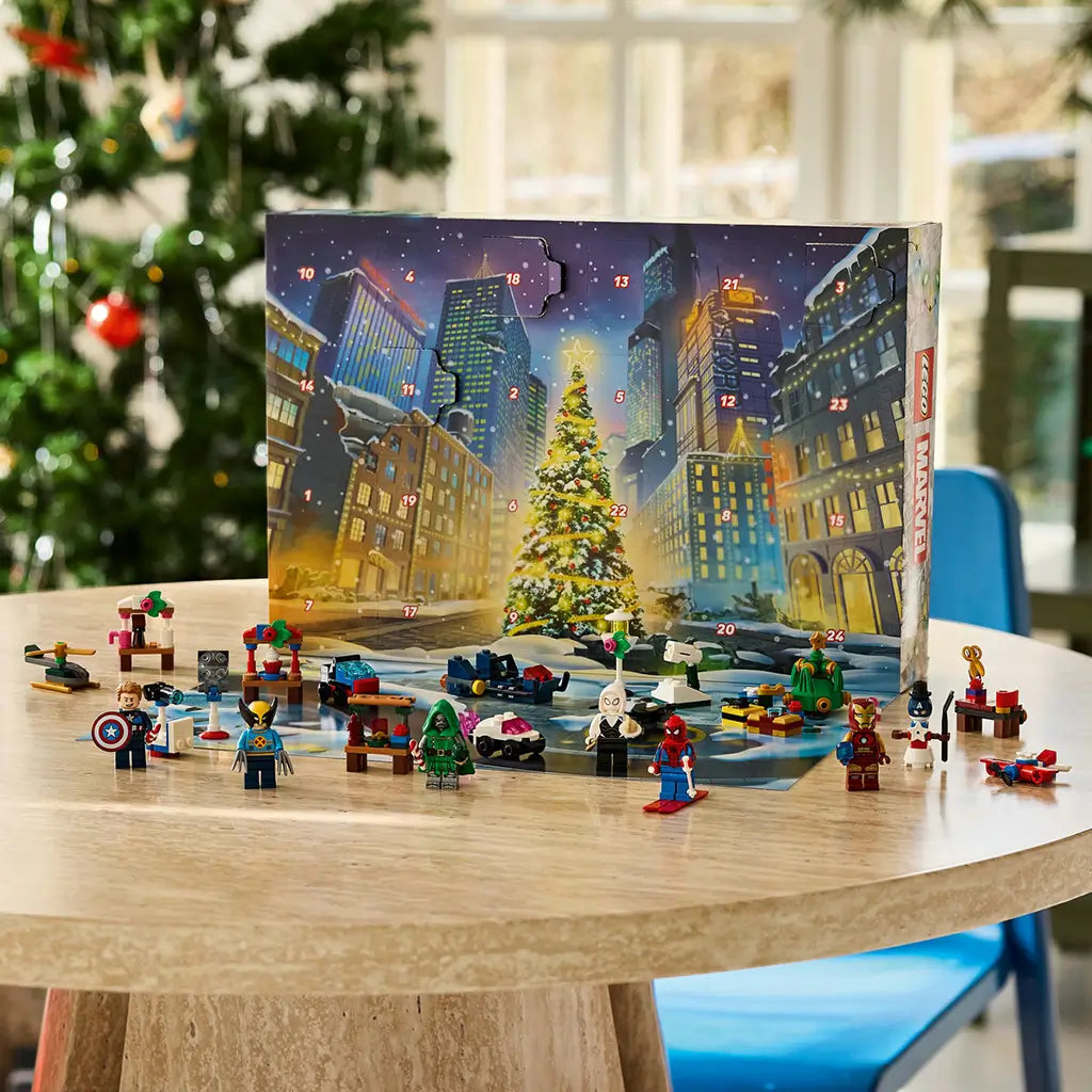 LEGO Marvel Advent Calendar 2026 display features colorful superhero minifigures and mini builds arranged before a snowy city calendar and Christmas tree on a wooden table.