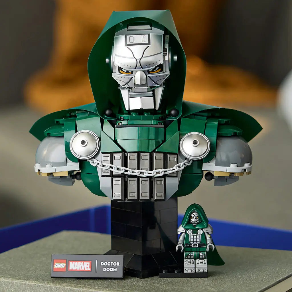 LEGO Marvel Doctor Doom Bust display model has a dark green hood, silver mask, gray armor and chain on a black base, with matching minifigure beside it in a home setting.