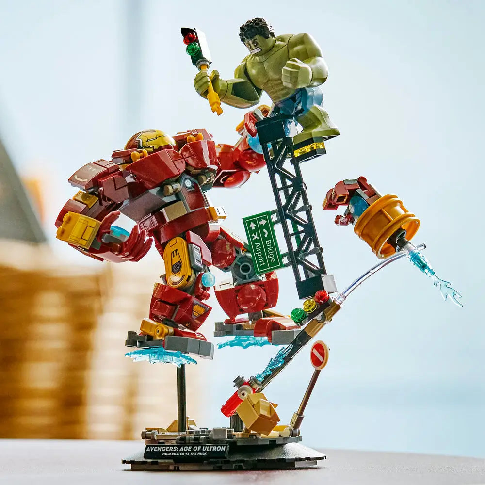 LEGO Marvel Hulkbuster vs Hulk lifestyle display shows the completed red and gold Hulkbuster mid-action against the green Hulk, mounted on a dynamic base with street elements and Avengers branding.