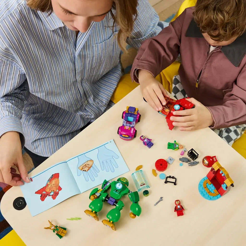 LEGO Marvel Loki vs. Team Iron Man pieces in red, green, purple, and gold plastic are assembled at a table by an adult and child using illustrated instructions.