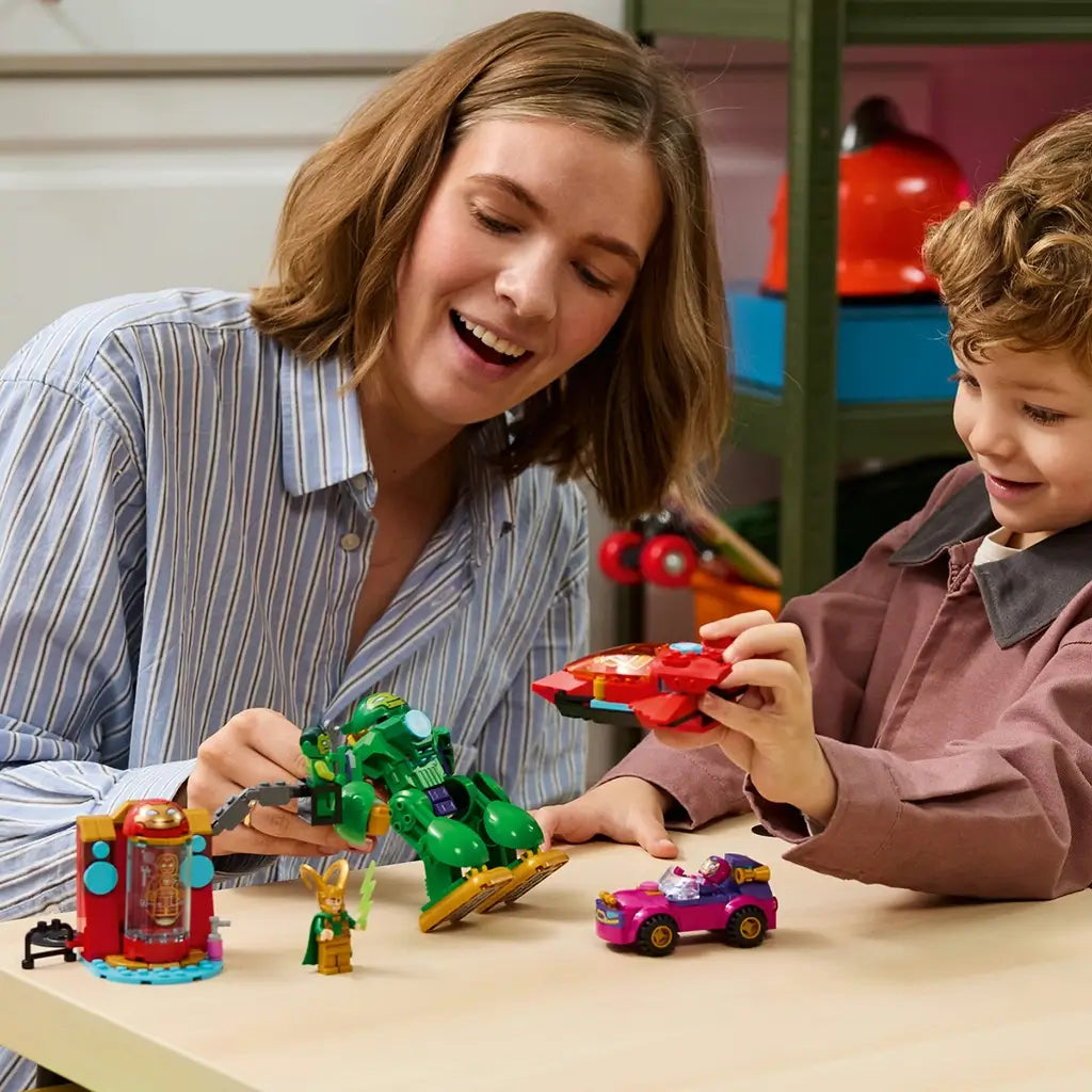LEGO Marvel Loki vs. Team Iron Man playset in colorful plastic is used by an adult and child, who hold the green Iron Hulk mech and red jet beside the car and Loki.
