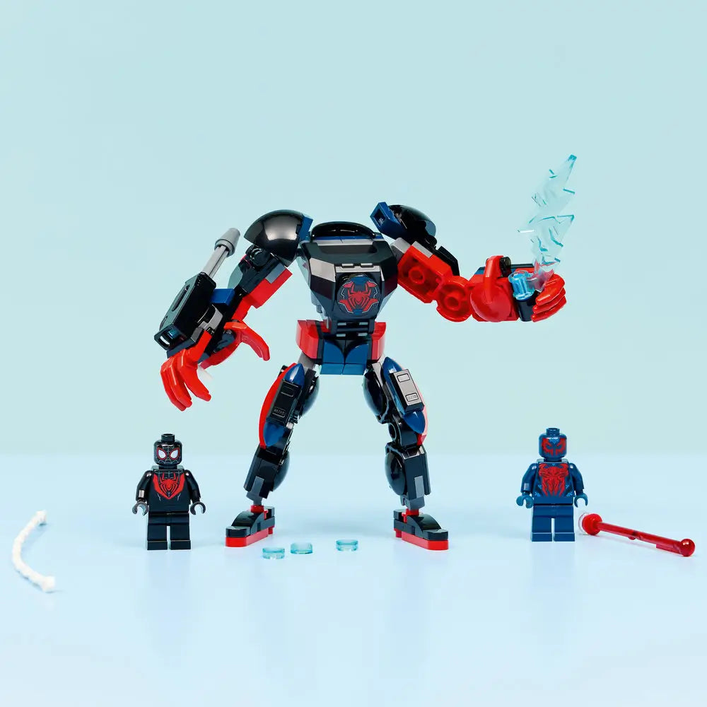 LEGO Marvel Spider-Man mech display setup with black, red, and blue articulated robot standing upright, flanked by two minifigures and web elements, photographed on a minimal light blue studio surface.