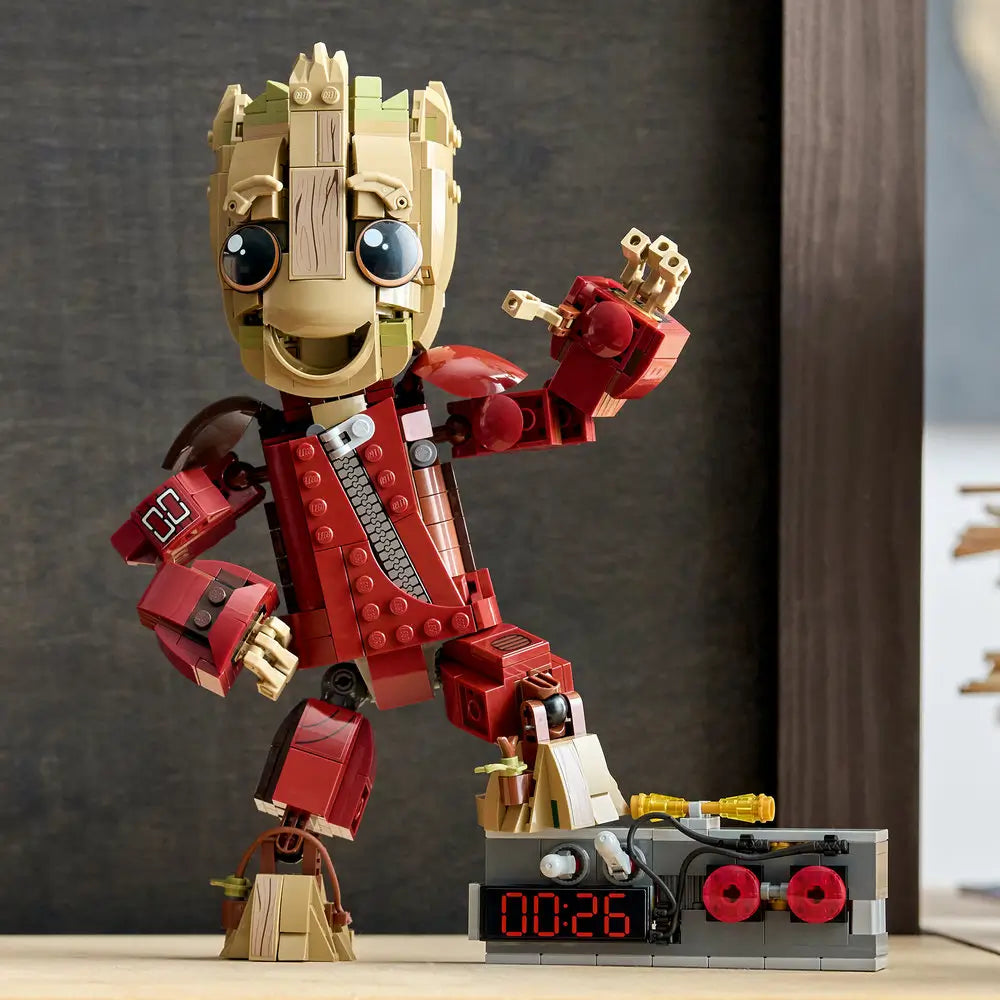 LEGO Marvel Ravager Jumpsuit Groot display shows the finished tan and brown Groot figure posed dynamically on a surface, wearing a red jumpsuit and standing next to a detailed gray detonator build.