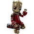 LEGO Marvel Groot buildable figure shows tan and light brown wood-textured bricks forming a smiling Groot character wearing a dark red Ravager jumpsuit, posed standing beside a gray detonator base on a neutral background.