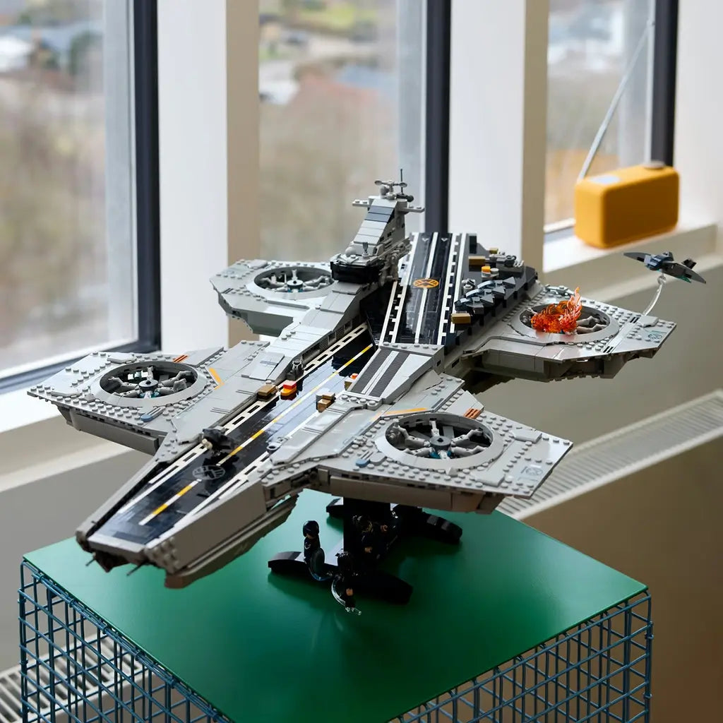 LEGO Marvel S.H.I.E.L.D. Helicarrier display model, gray plastic aircraft-carrier build with detailed deck and rotor sections, showcased on a stand near large windows in a modern interior.