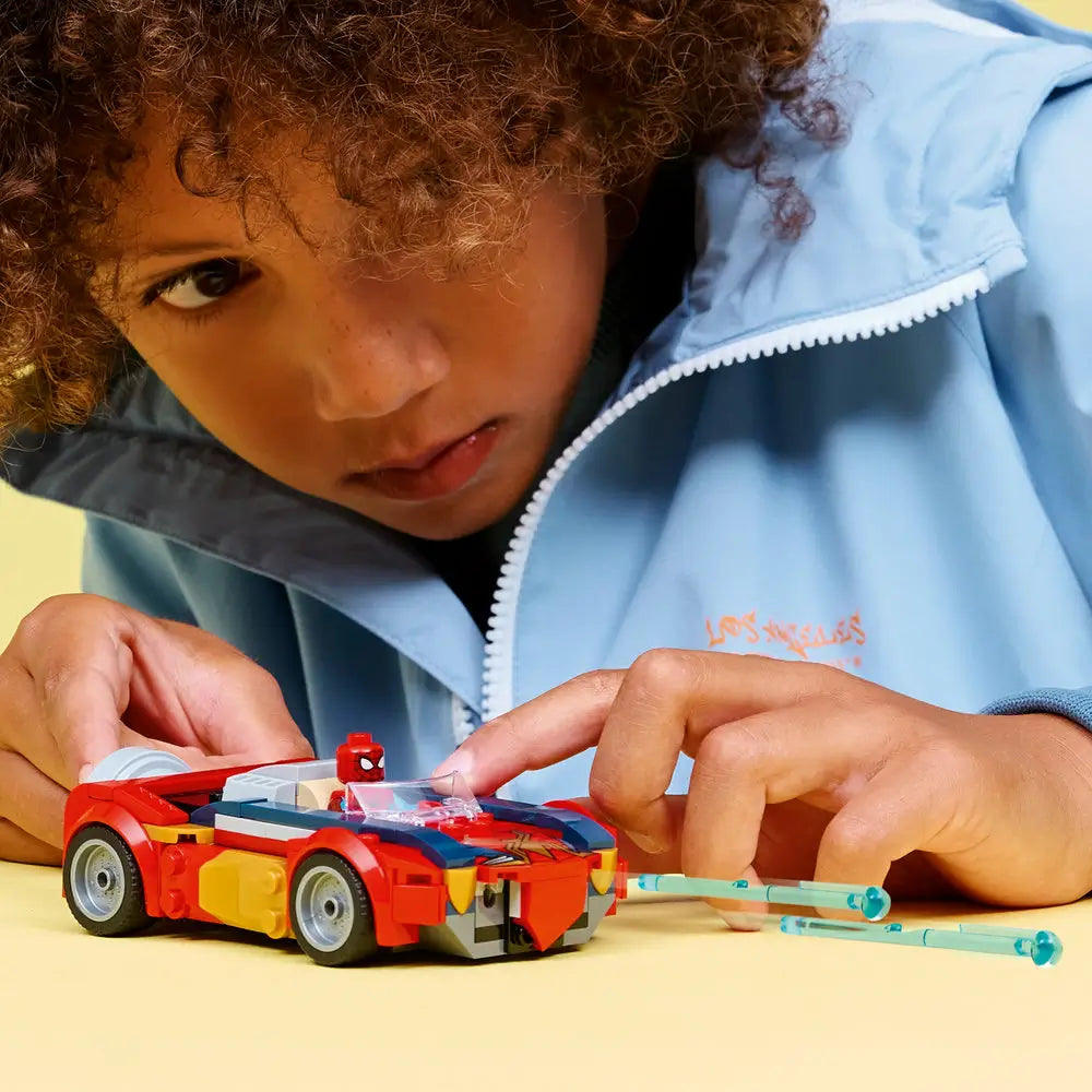 LEGO Marvel Spider-Man car play scene showing a child pushing the red and blue vehicle with translucent web blasts, highlighting rolling wheels, cockpit details, and imaginative hands-on play on a yellow background.