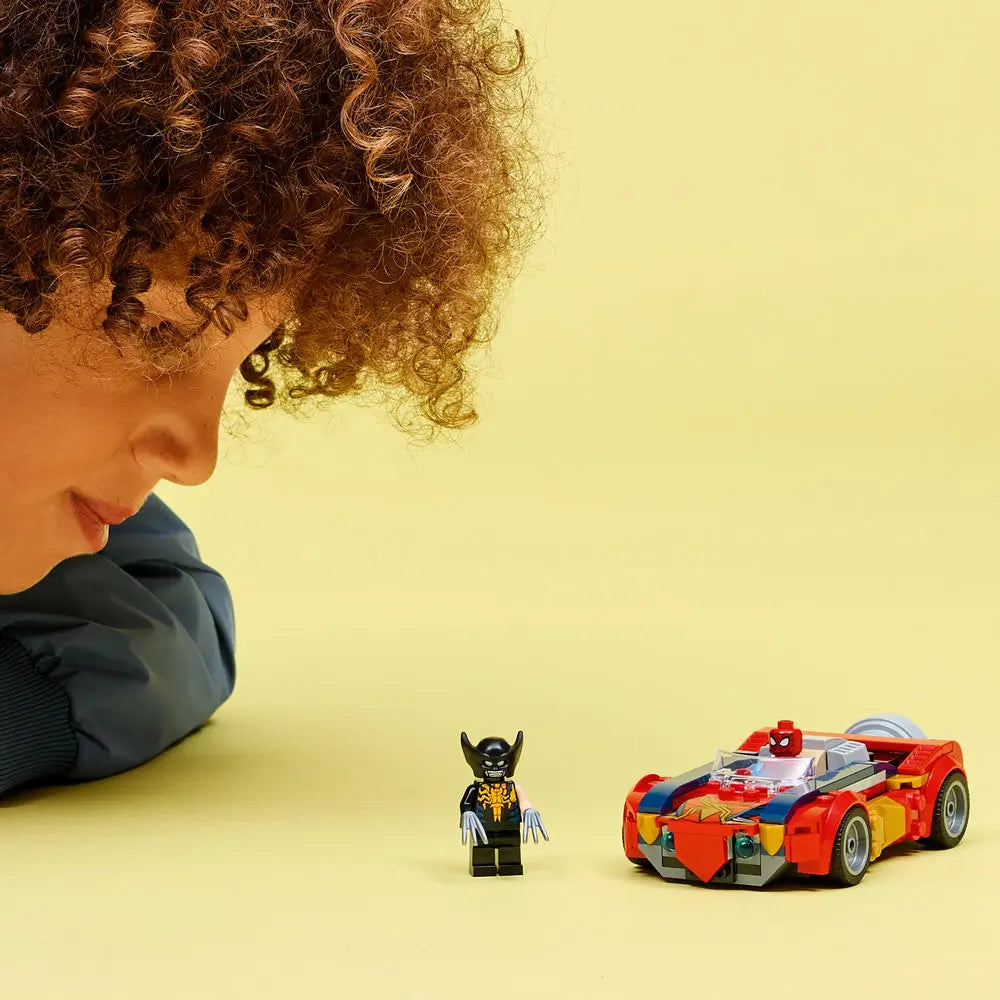 LEGO Marvel Spider-Man car display with red, blue, and gold vehicle parked beside Venomized Wolverine minifigure, photographed on a bright yellow studio surface to show scale, characters, and accessories.