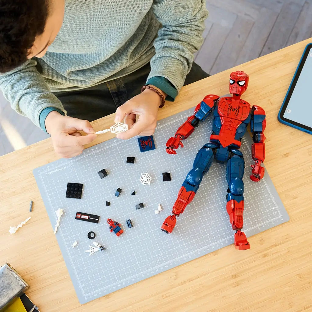 LEGO Marvel Spider-Man construction set, red and blue plastic articulated figure with detachable accessories and web elements, shown during assembly on a cutting mat workspace.