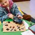 LEGO Marvel building experience, blue plastic prison transport truck components, minifigures, wheels and accessories arranged during hands-on assembly beside a tablet and drawing sheet.