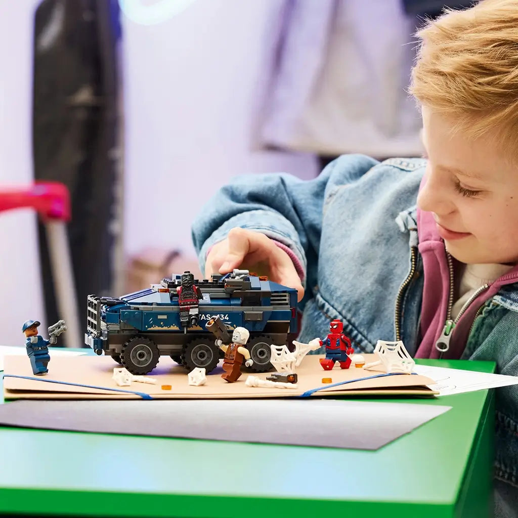 LEGO Marvel Spider-Man playset, blue plastic armored prison truck with rugged body panels and action features, displayed with minifigures as a child recreates superhero chase scenes indoors.