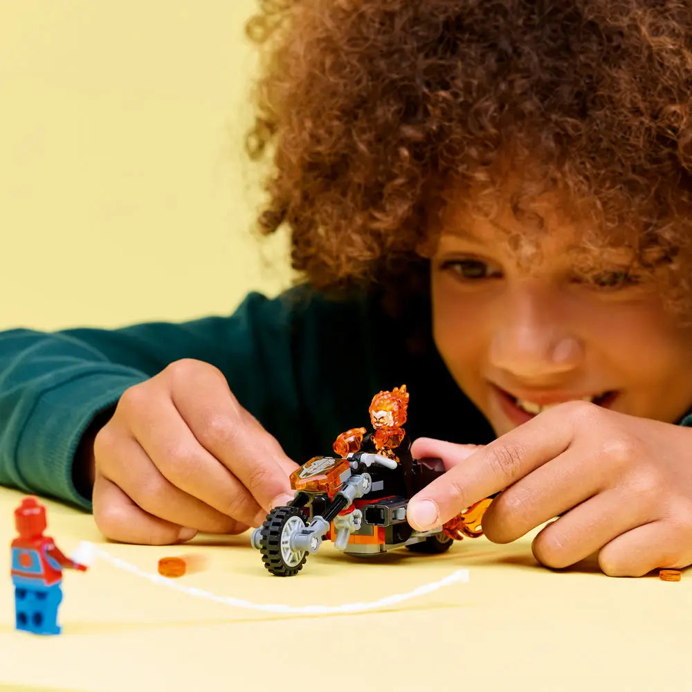 LEGO Marvel Ghost Rider motorcycle play scene showing a child pushing the flame-covered bike with rolling wheels and translucent fire details, highlighting hands-on action play and character interaction on a bright yellow background.