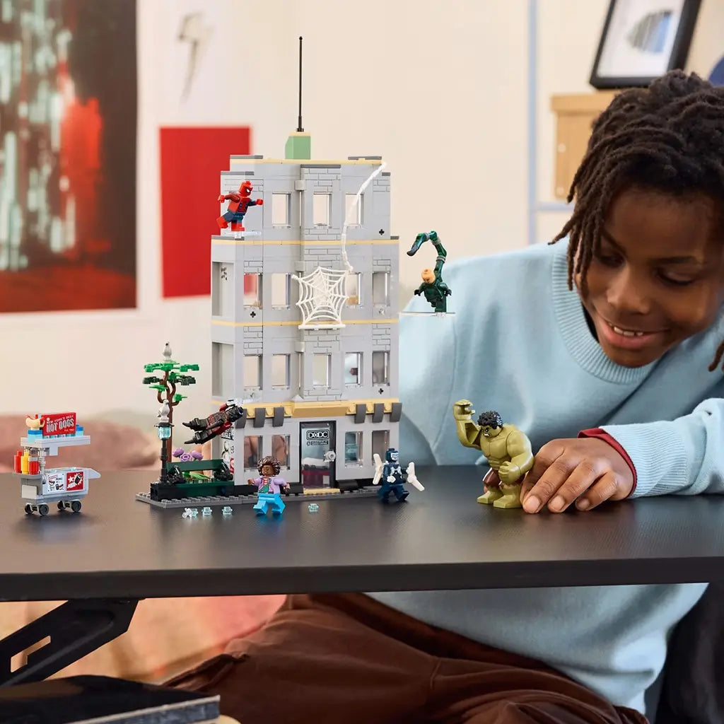 LEGO Marvel Spider-Man playset, gray plastic multi-story building with web details and villain figures, displayed on a tabletop as a child poses Hulk during imaginative superhero action scenes.
