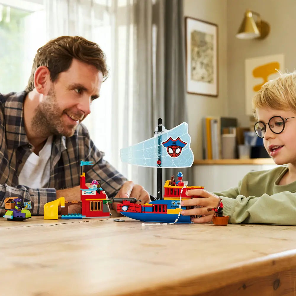 LEGO Marvel Spidey pirate ship lifestyle image shows a parent and child smiling while assembling the colorful plastic ship and dock, demonstrating shared building, storytelling play, and hands-on learning at home.