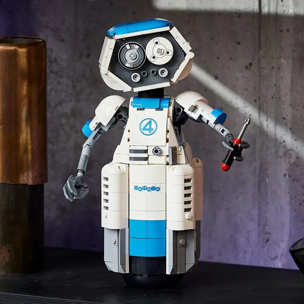 LEGO Marvel H.E.R.B.I.E. robot in white, blue and gray plastic bricks with articulated arms and a handheld tool, displayed upright on a dark table by a concrete wall.