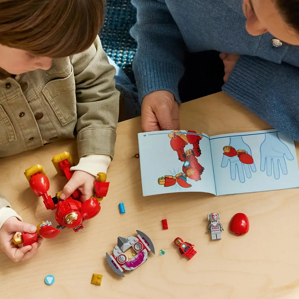 LEGO Marvel Ultron vs. Iron Man pieces in red, gold, gray, and pink plastic are assembled by a child at a table while an adult holds open illustrated build instructions.