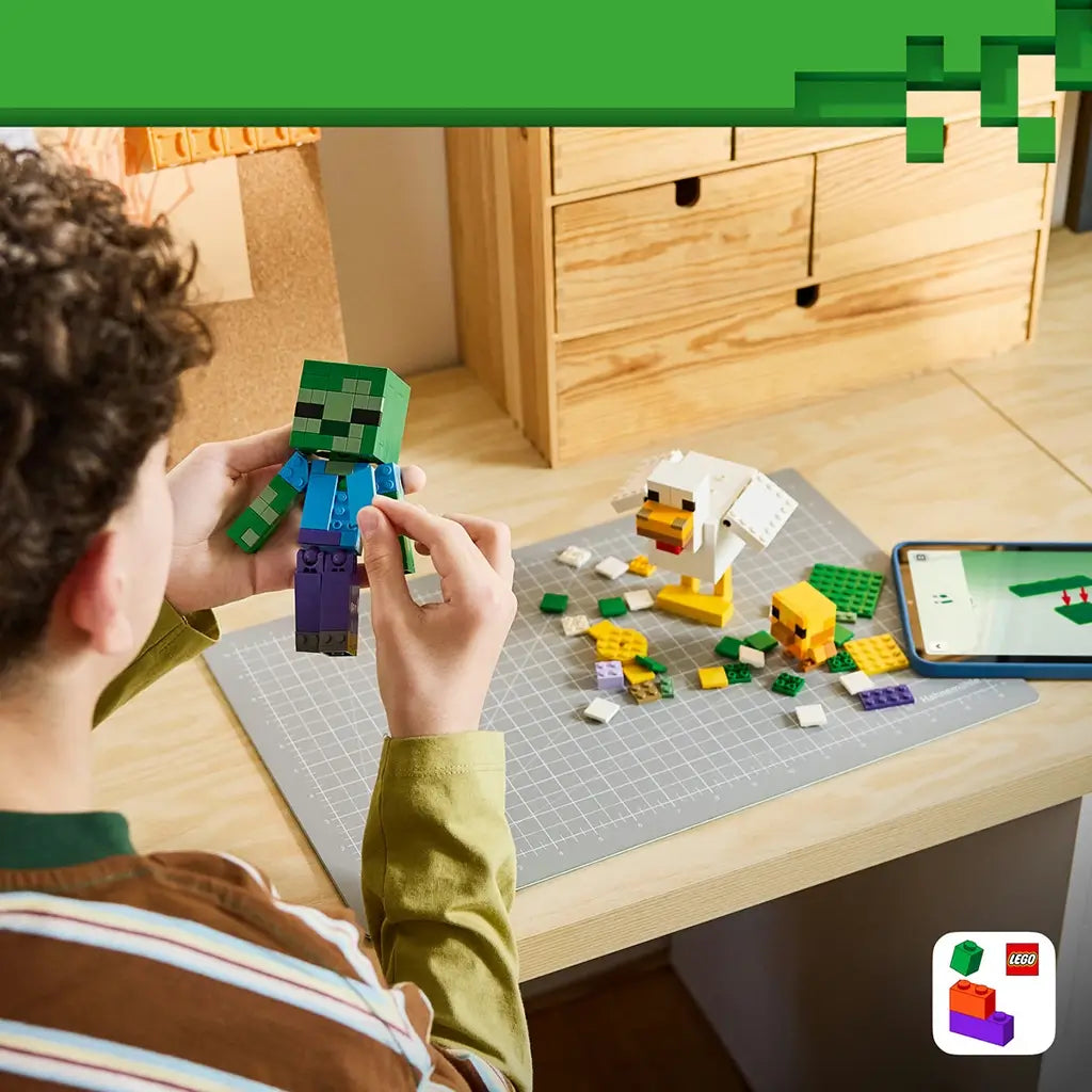 LEGO Minecraft Chicken Jockey building scene shows a builder holding a green zombie above a gray craft mat with a white chicken, yellow chick, loose bricks and a tablet.