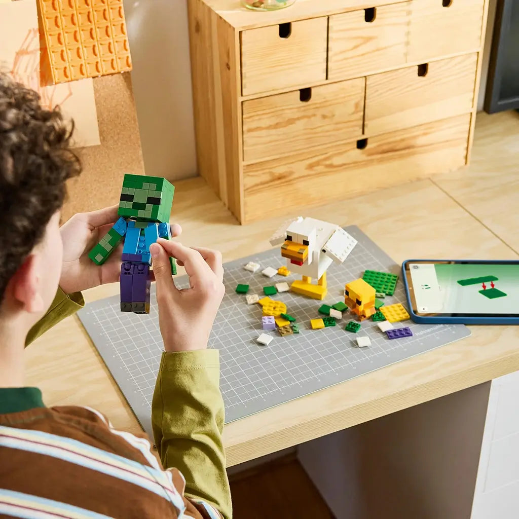 LEGO Minecraft Chicken Jockey building set uses green, white and yellow bricks as a builder assembles the zombie beside a chicken, chick, loose pieces and digital instructions.