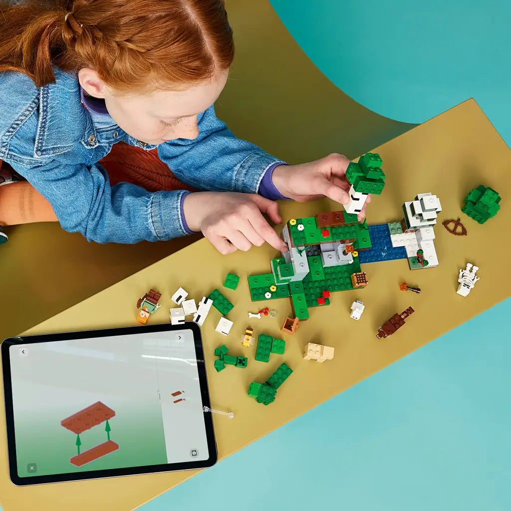 LEGO Minecraft First Night Adventure build in green, white and brown bricks is assembled by a child at a table with loose pieces and digital instructions on a tablet.