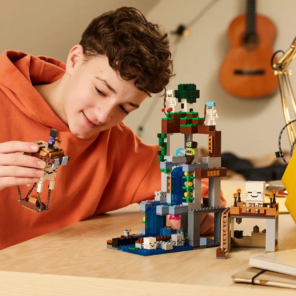 LEGO Minecraft Ghast Station in gray, brown, green and blue bricks stands on a wooden table as a smiling child plays with a suspended ghast and character figure.