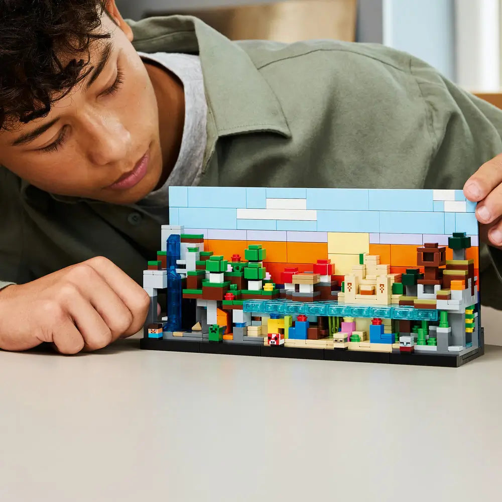LEGO Minecraft building scene shows hands assembling colorful plastic blocks into small terrain modules on a tabletop beside a tablet displaying step-by-step digital building instructions.