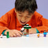 LEGO Minecraft Steve’s Taiga Adventure lifestyle builder image showing a child assembling white, green, and gray plastic bricks, blocky cubic forms for creative play, following digital instructions with figures and accessories spread out.