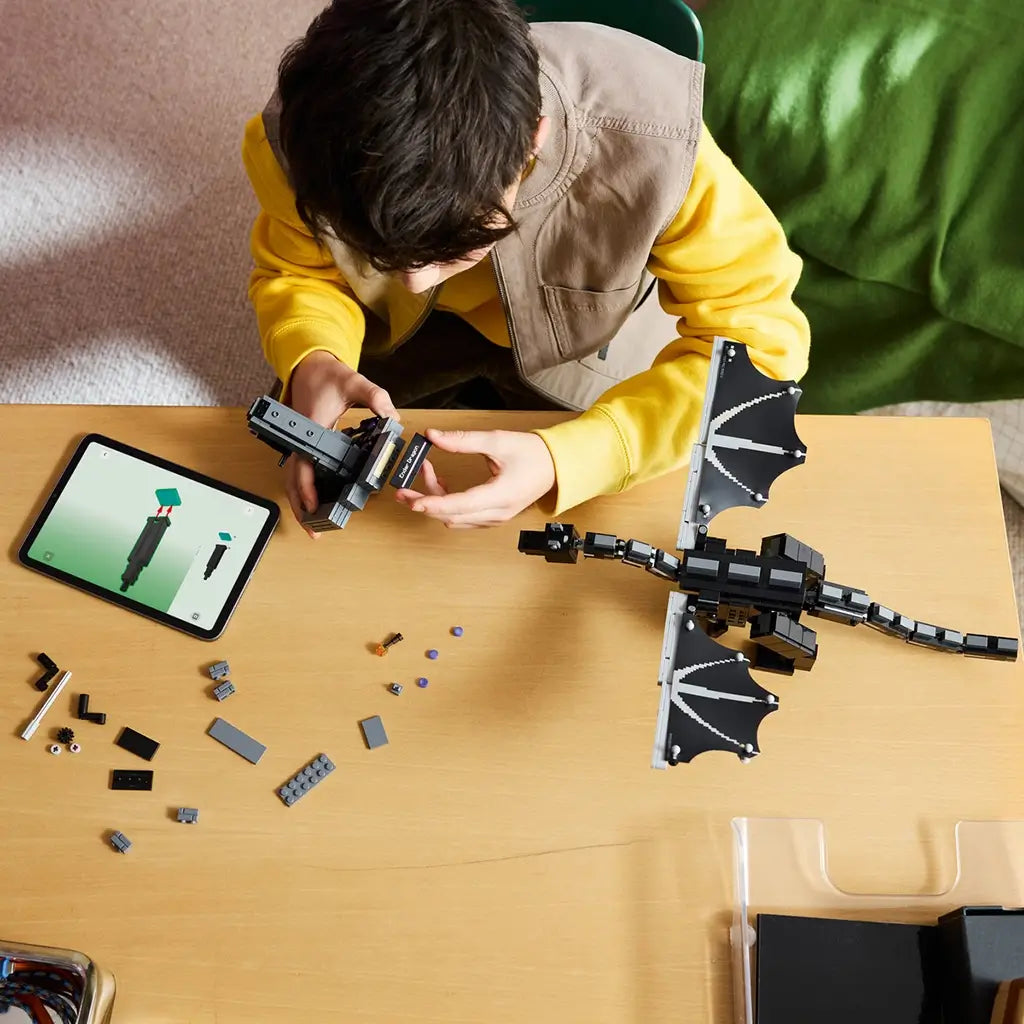 LEGO Minecraft The Ender Dragon build in black and gray bricks is assembled by a child at a table with loose pieces and digital instructions beside the winged model.