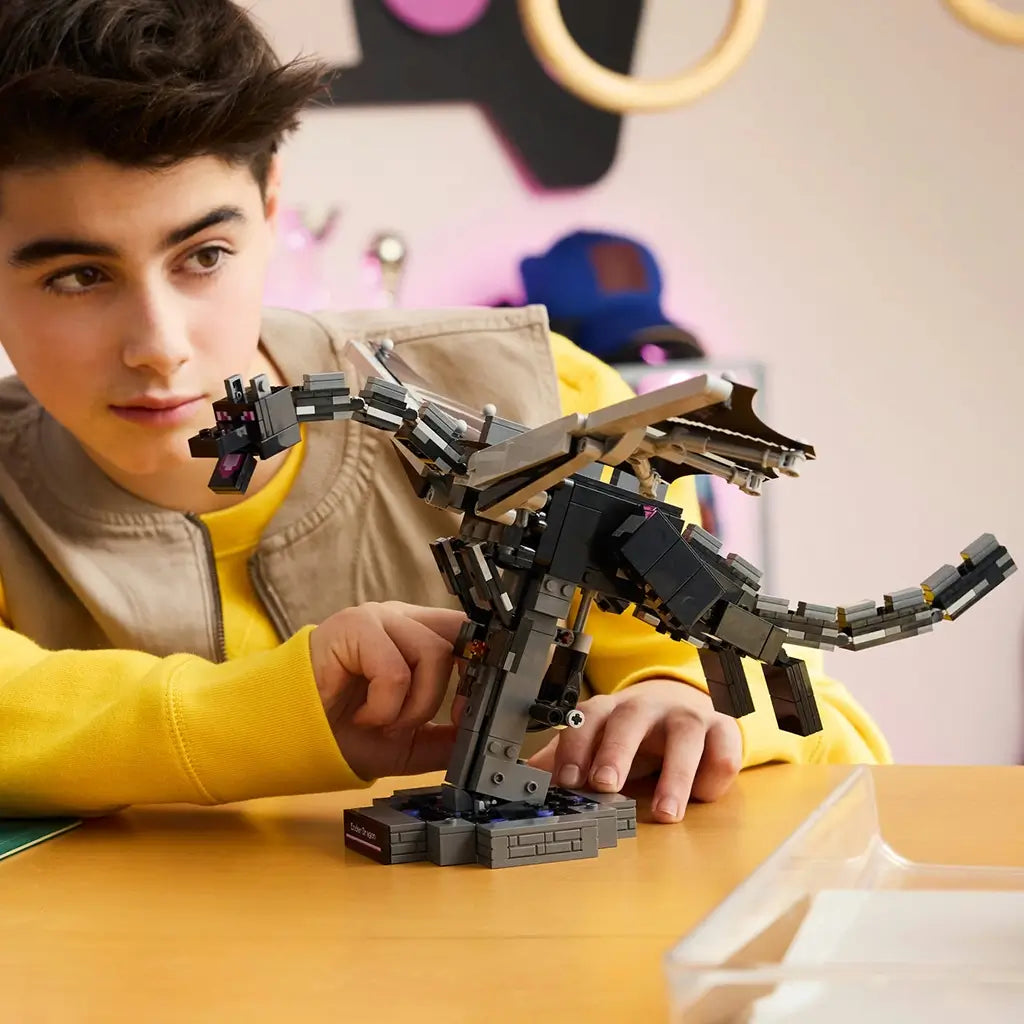 LEGO Minecraft The Ender Dragon model in black and gray bricks is adjusted by a child at a table, showing its articulated wings, segmented tail and dark display stand.