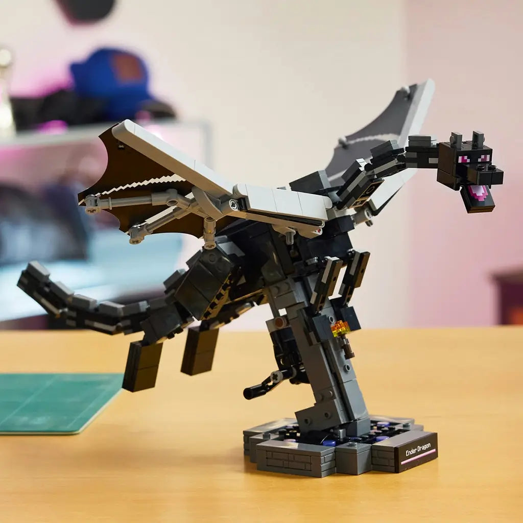 LEGO Minecraft The Ender Dragon model in black and gray bricks spreads articulated wings above a dark display stand on a tabletop, with a softly blurred room behind.