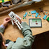 LEGO Minecraft The Skeleton model in white and gray bricks is assembled by a person at a wooden table, with turquoise pieces and digital building instructions nearby.